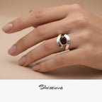 Silver ring with a red gemstone on a hand, branded 'Silvassions'.