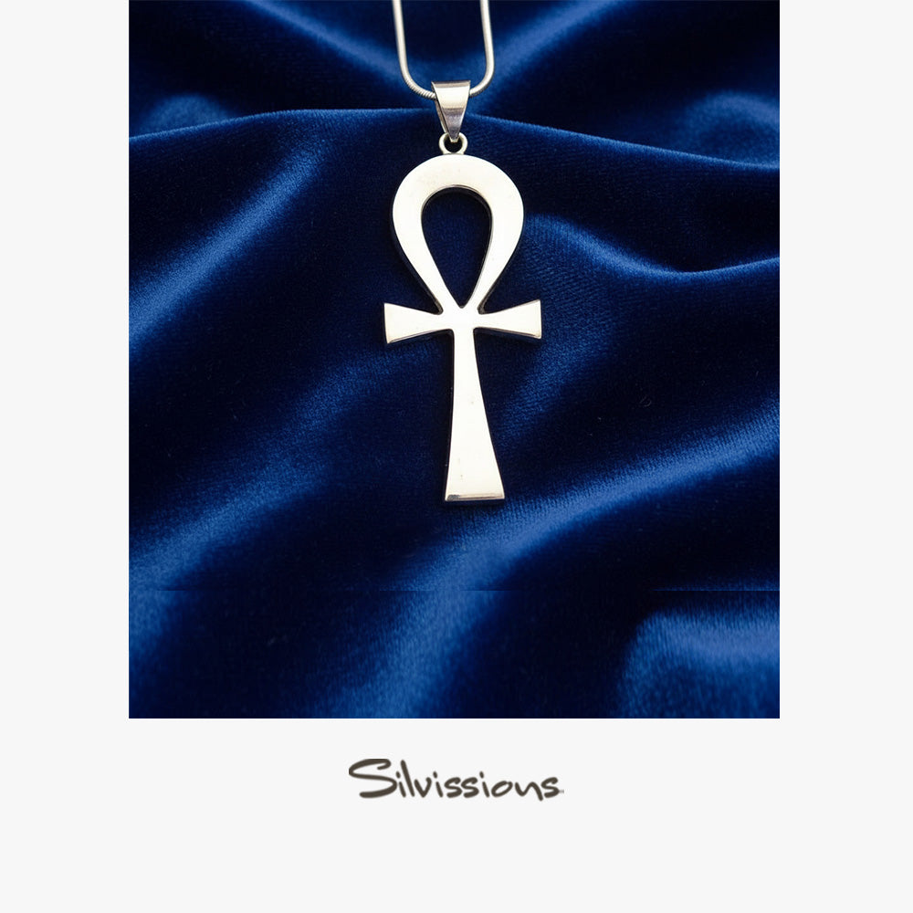 Silver ankh pendant on a blue satin background with 'Silviassins' branding.