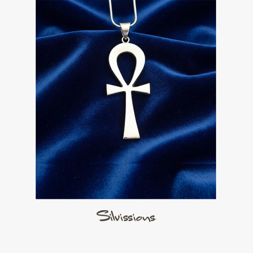 Silver ankh pendant on a blue satin background with 'Silviassins' branding.
