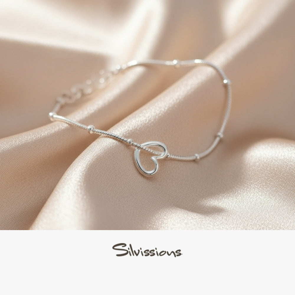 Silver ankle bracelet with heart charm on a soft fabric background, featuring the brand 'Silvissions'.