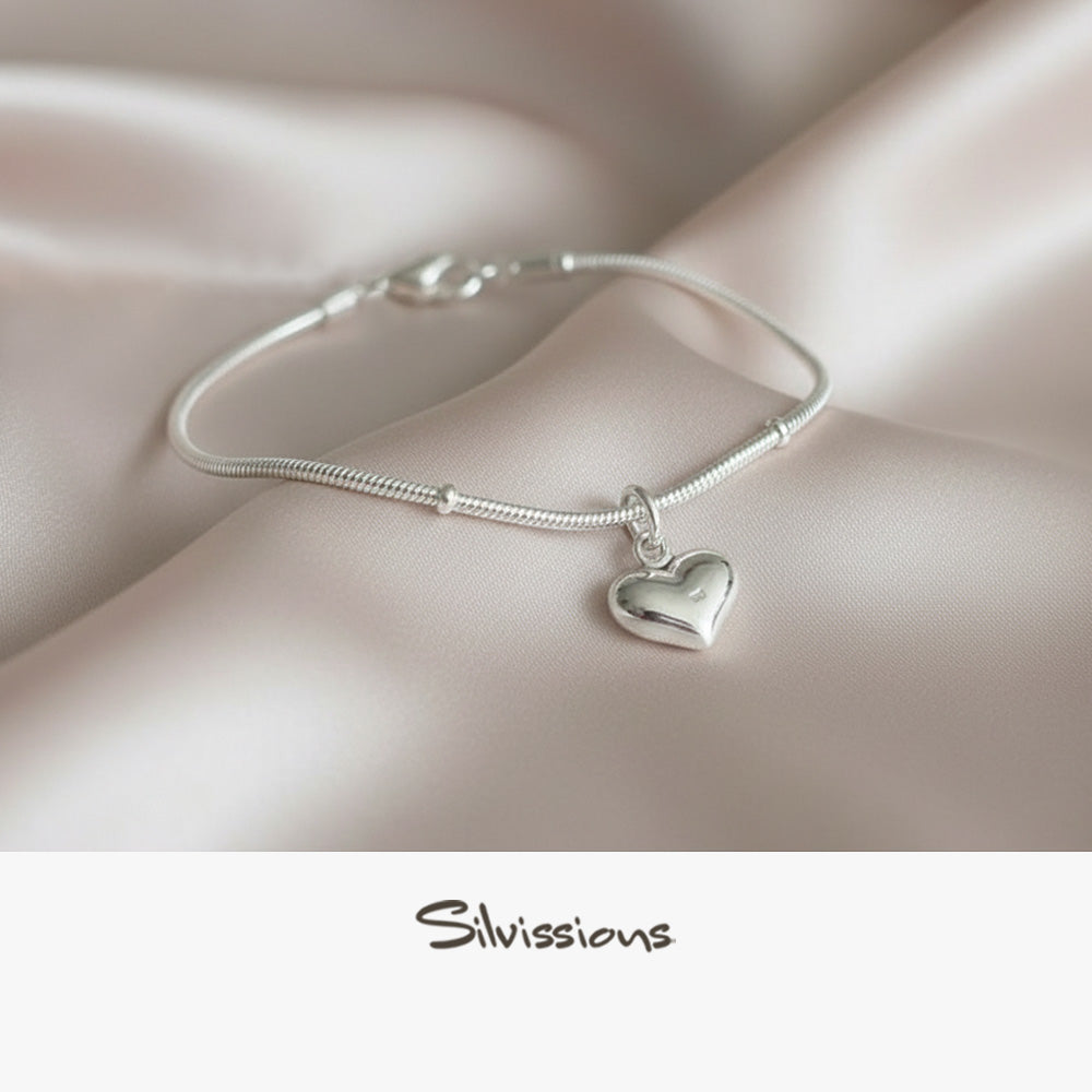Silver ankle bracelet with a heart charm on a soft fabric background, featuring the brand 'Silvissions'.