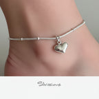 Silver ankle bracelet with a heart-shaped charm on a blurred background, featuring the brand 'Silvissions'.