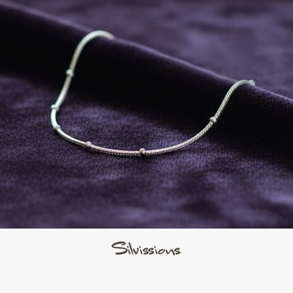 Silver ankle bracelet on a dark fabric background with 'Silvissions' branding.
