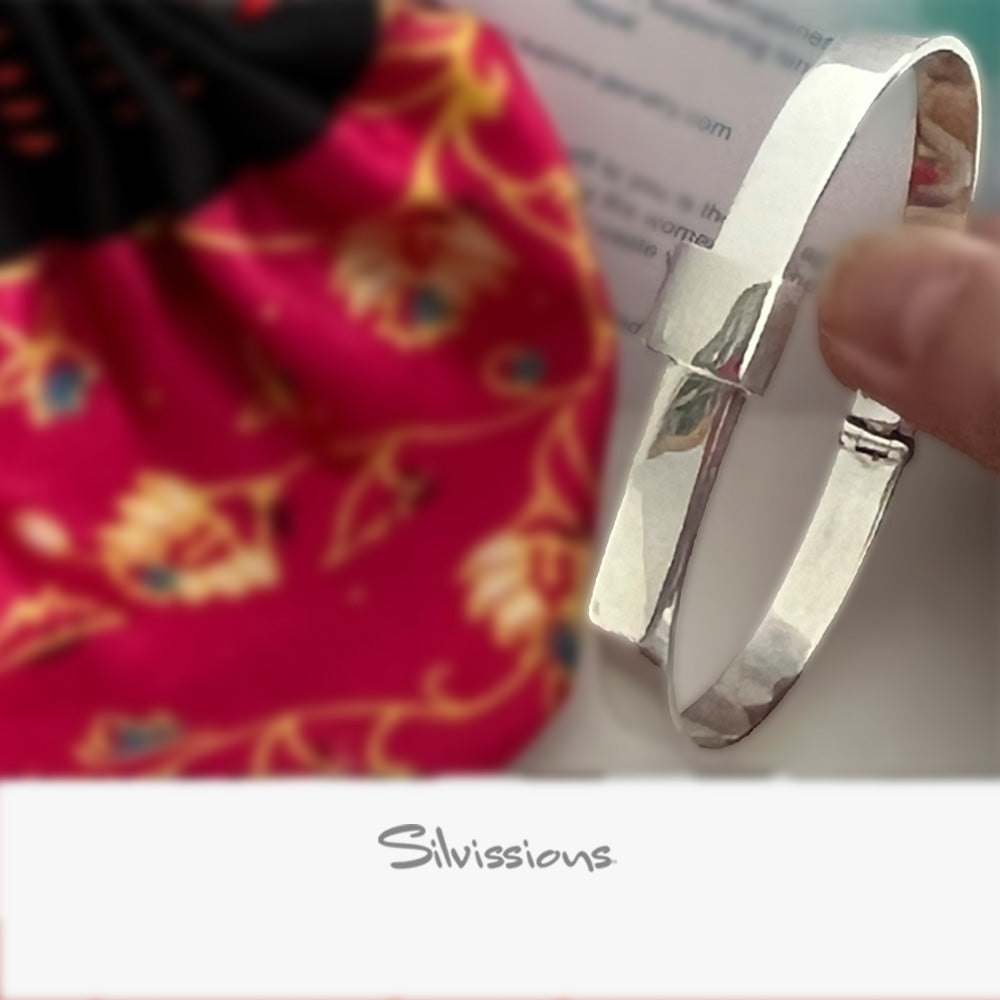 Silver bracelet held by a hand with a colorful fabric background