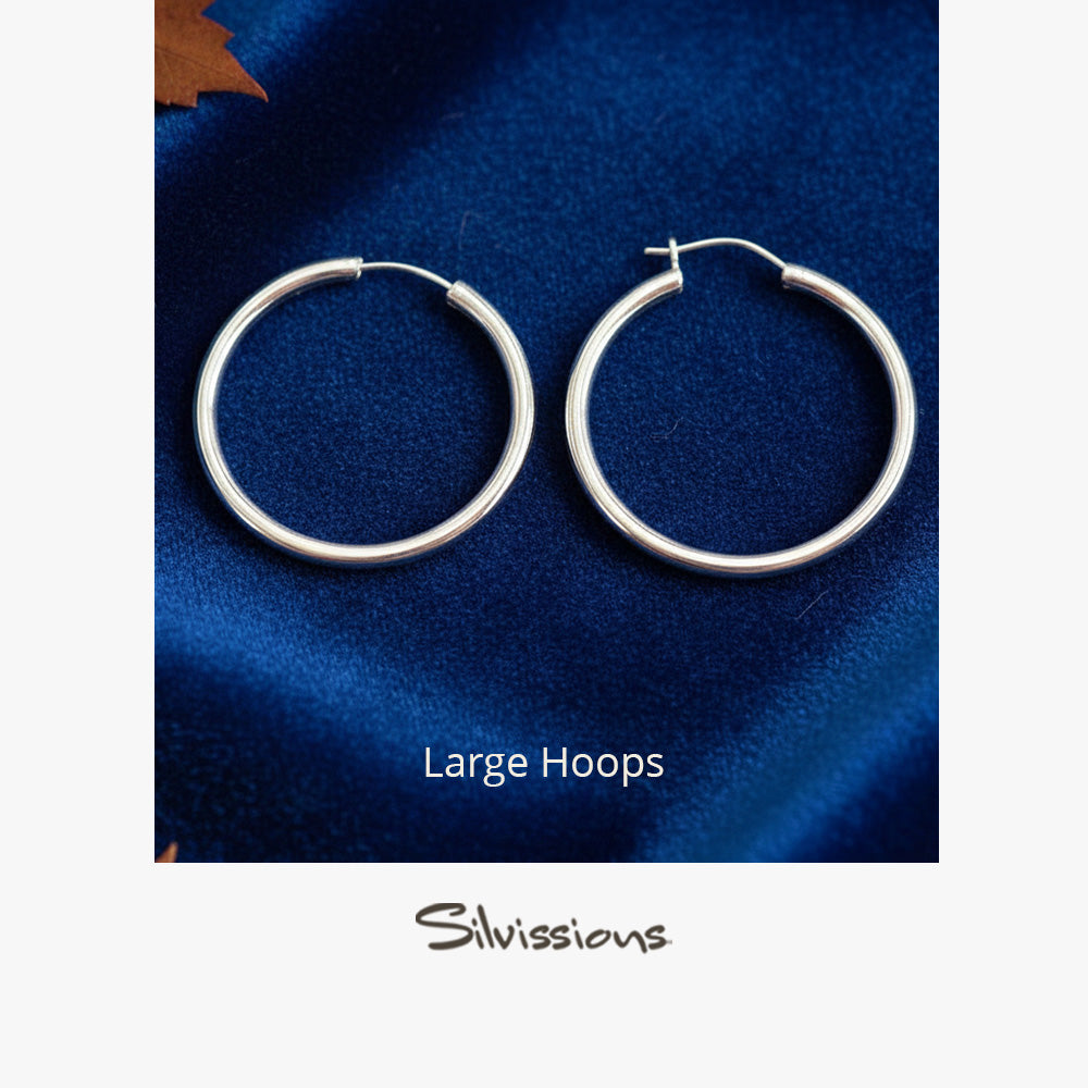 Pair of silver hoop earrings on a blue fabric background with 'Silvissions' branding.