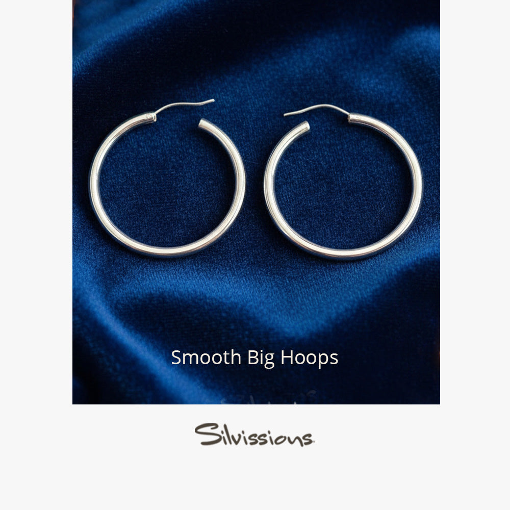 Pair of silver hoop earrings on a blue fabric background with 'Silvissions' branding.