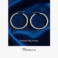 Pair of silver hoop earrings on a blue fabric background with 'Silvissions' branding.