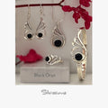 Silver jewelry set with black onyx gemsstones including earrings, a ring, and a bracelet, displayed against a neutral background.