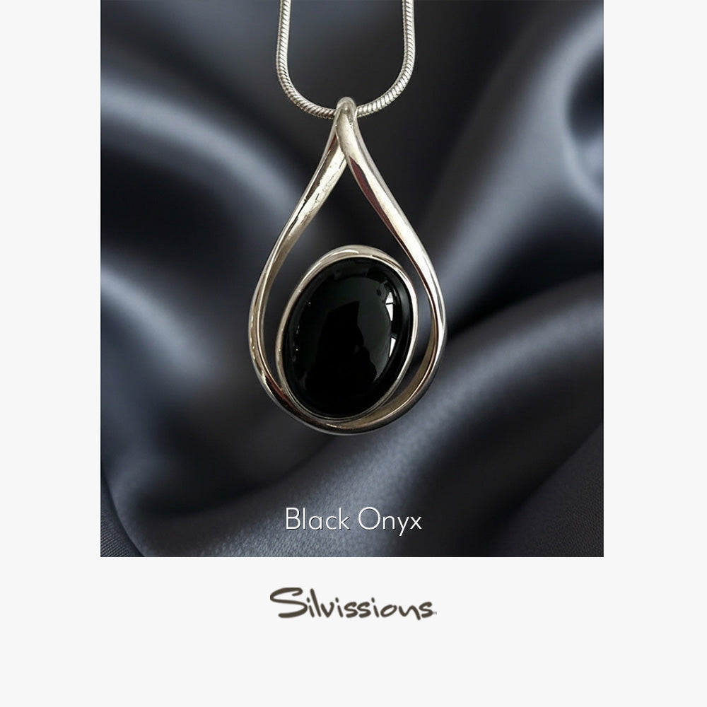 Black onyx pendant in a silver setting on a dark fabric background, with 'Silvissions' branding.