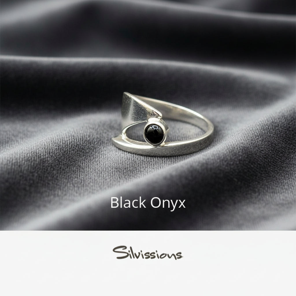 Silver ring with black onyx stone on gray fabric, branded 'Silvissions'.