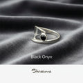 Silver ring with black onyx stone on gray fabric, branded 'Silvissions'.