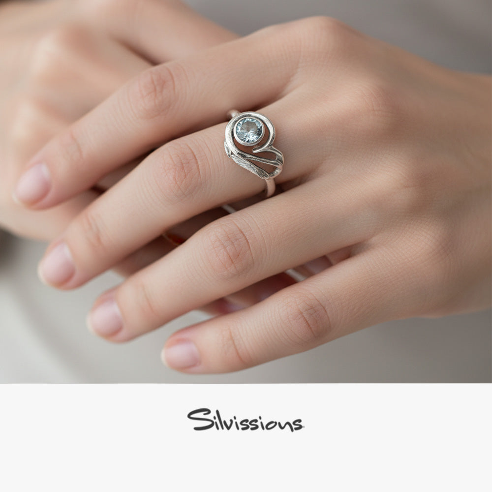 Silver ring with a blue topaz gemstone on a hand, branded 'Silvissions'.