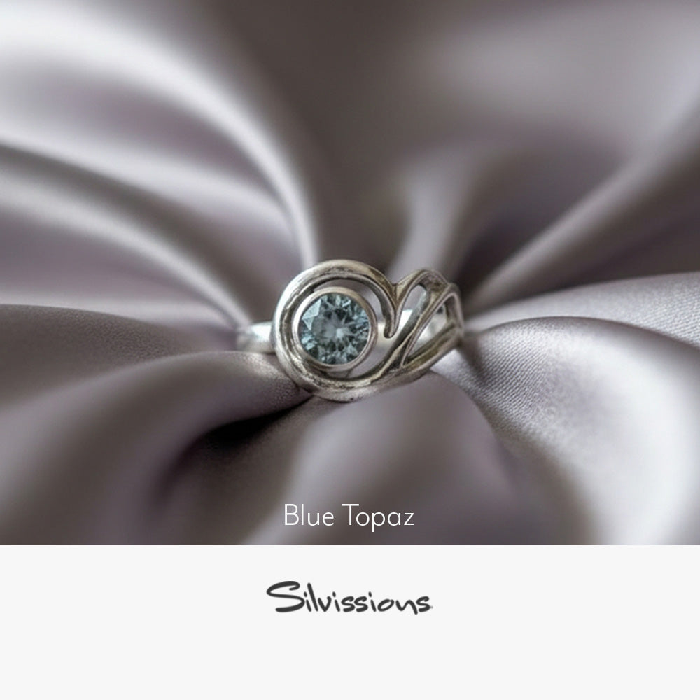 Silver ring with blue topaz gemstone on a neutral background, featuring the brand 'Silvissions'.