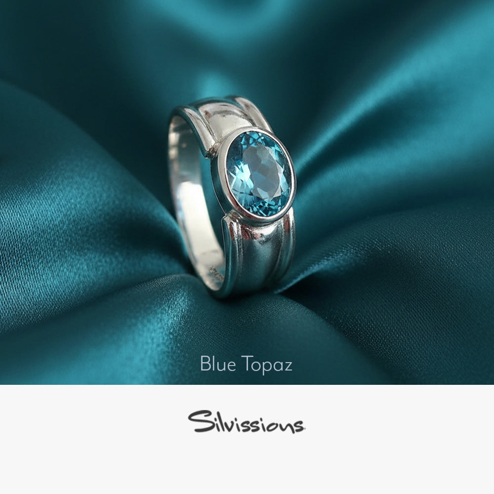 Silver ring with blue topaz gemstone on teal satin fabric, featuring the brand 'Silvissions'.