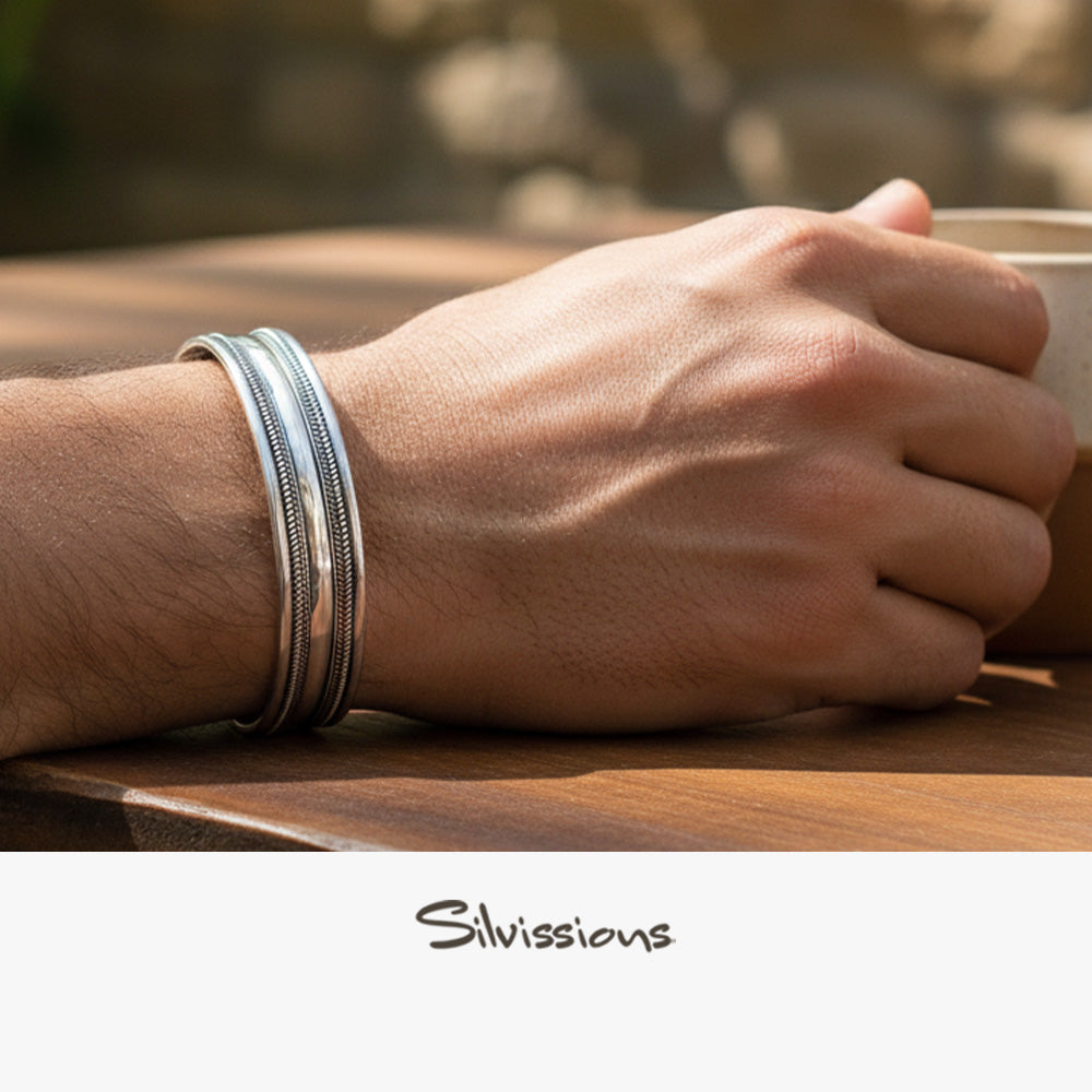 Hand wearing silver bracelets holding a cup on a wooden surface with 'Silvissions' branding.