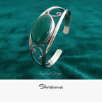 Silver bracelet with a green stone on a teal fabric background
