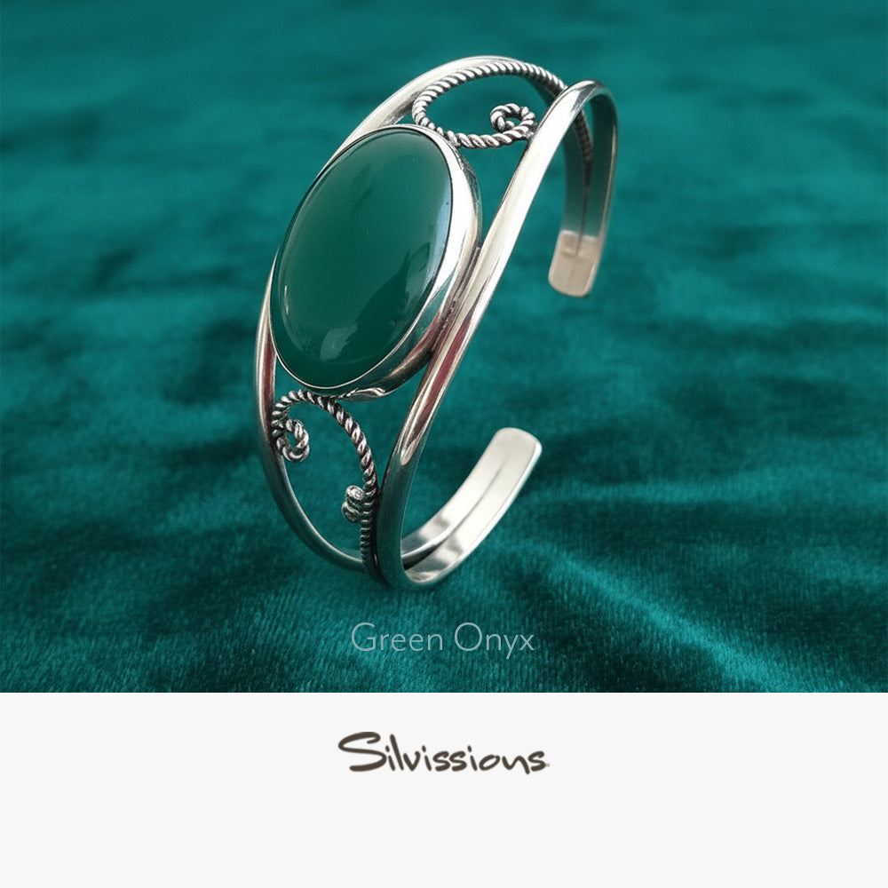 Silver bracelet with a green stone on a teal fabric background