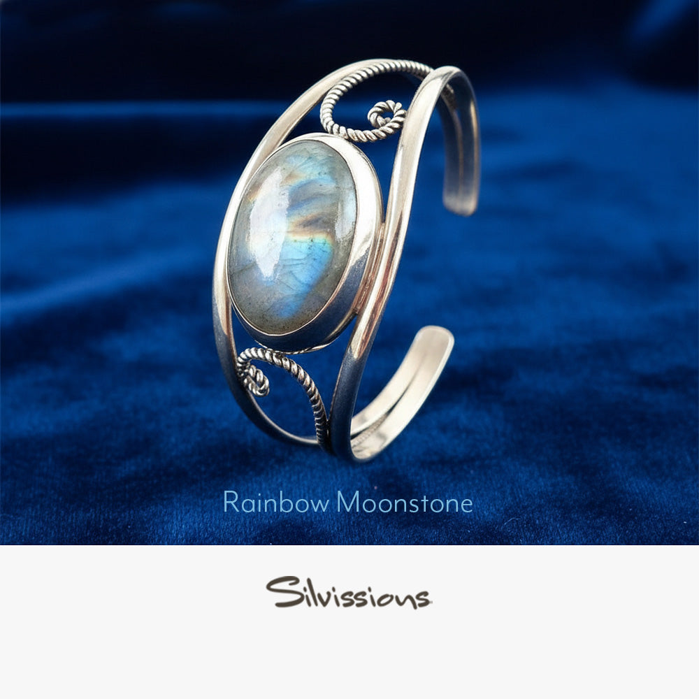 Silver bracelet with a rainbow moonstone gemstone on a blue fabric background, featuring the brand 'Silvissions'.
