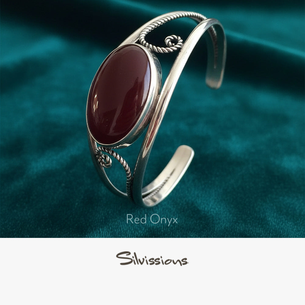 Silver bracelet with red onyx gemstone on a teal fabric background, featuring the brand 'Silvissions'.