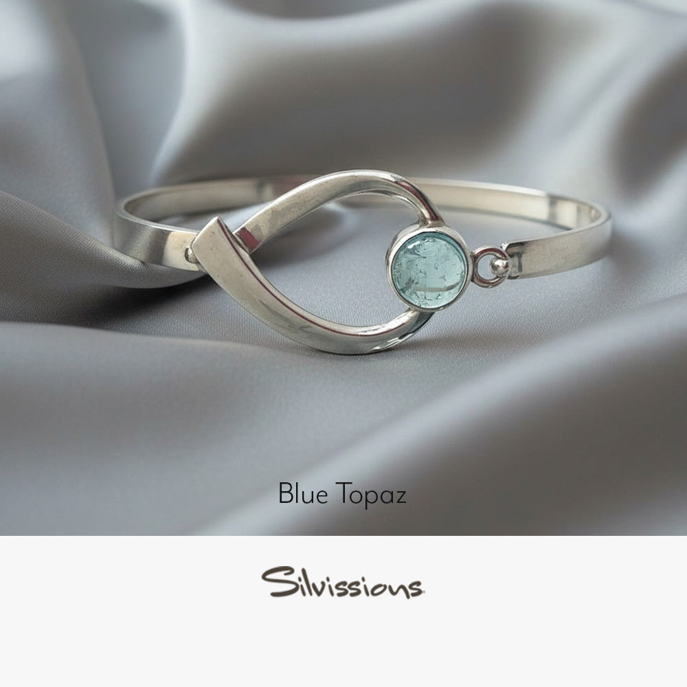 Silver bracelet with a blue topaz stone on a soft fabric background, featuring the brand 'Silvissions'.