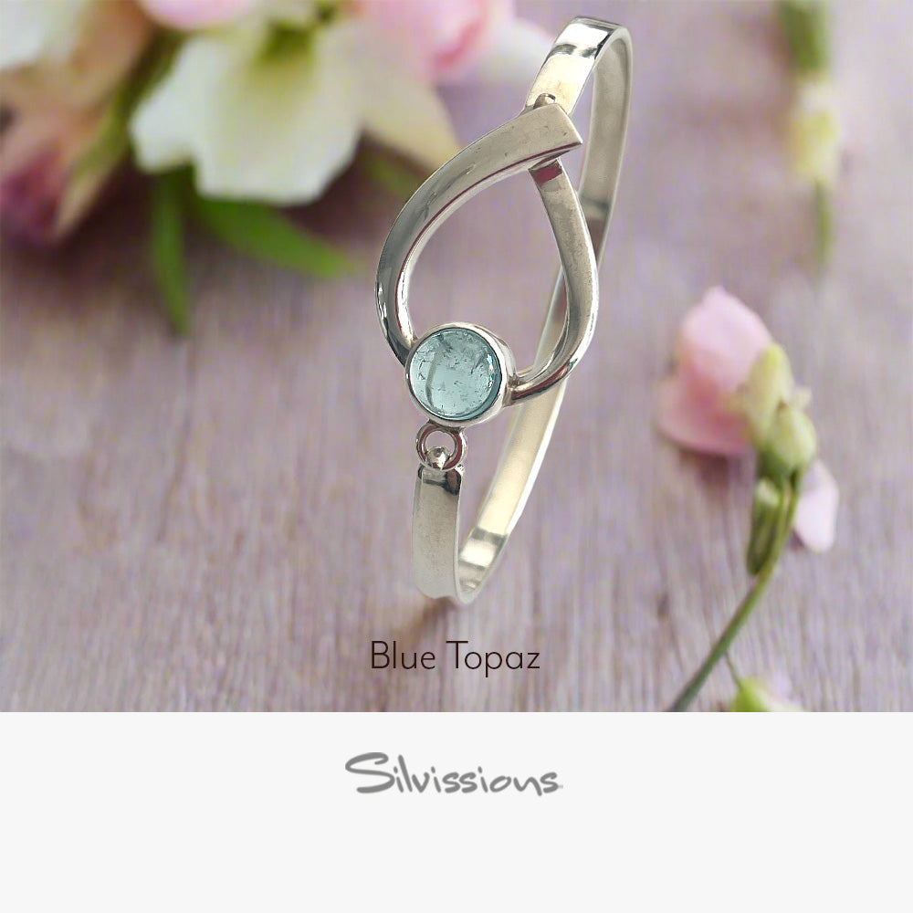 Silver bracelet with a green gemstone on a wooden surface with flowers