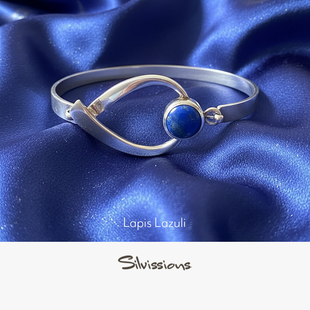 Silver bangle with a blue gemstone on a neutral background, featuring the brand 'Silvissions'.