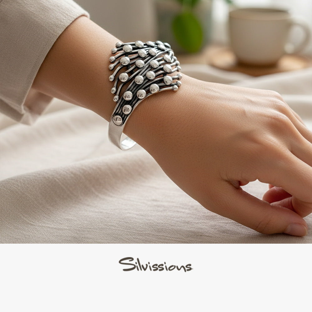 Silver bracelet on a wrist with a blurred background featuring a cup and plant.