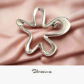 A sterling silver star-shaped brooch laid on a pink silky surface with 'Silvissions Jewelry' written in the caption.