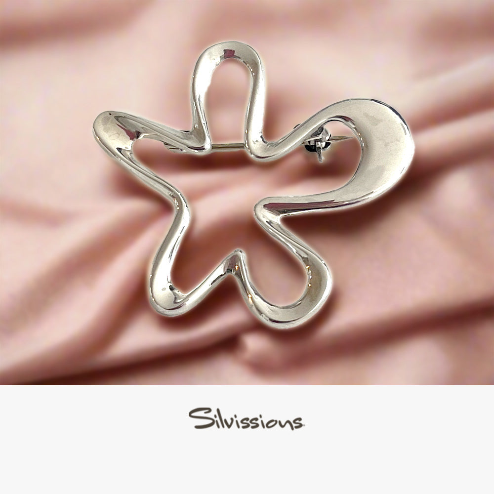 A sterling silver star-shaped brooch laid on a pink silky surface with 'Silvissions Jewelry' written in the caption.