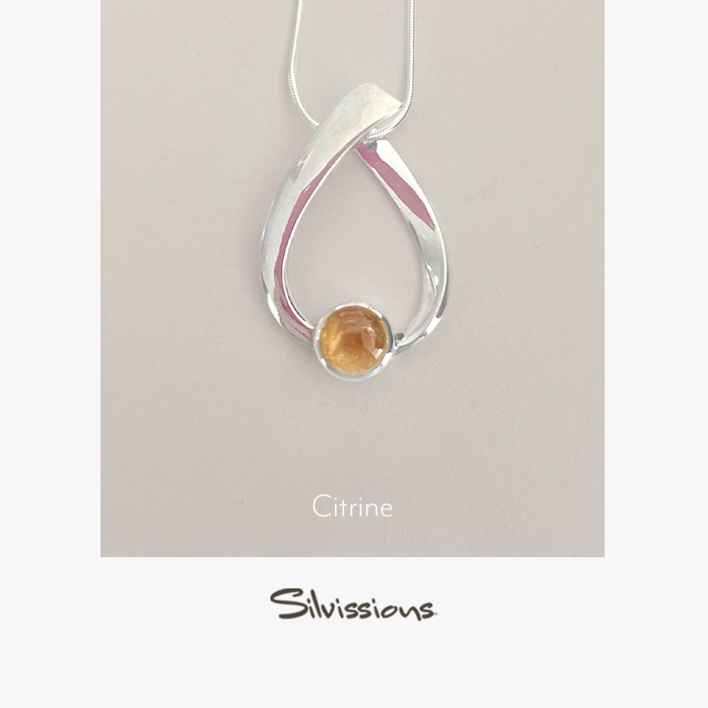 Silver pendant with a citrine stone on a beige background, branded 'Silvissions'.