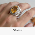 Silver ring with a yellow gemstone on a hand, branded 'Silvissions'.