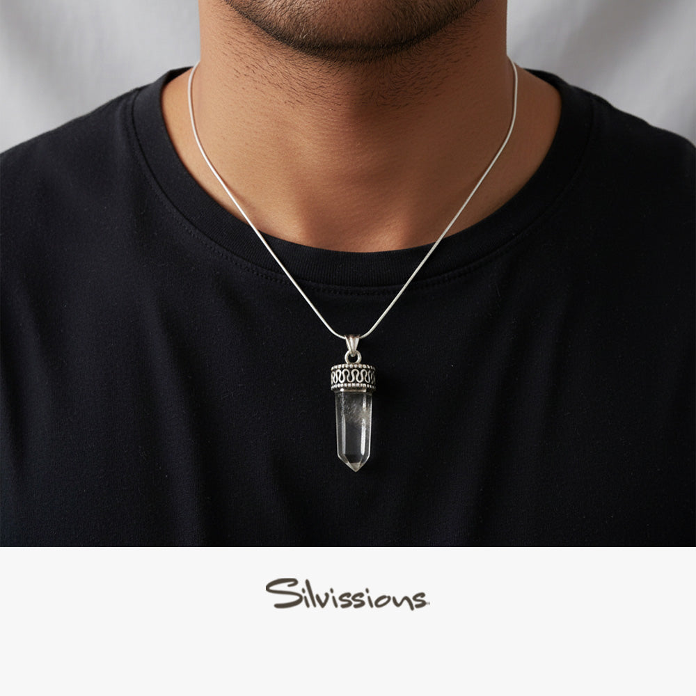 Person wearing a silver necklace with a clear crystal pendant on a plain background, featuring the brand 'Silviissions'.