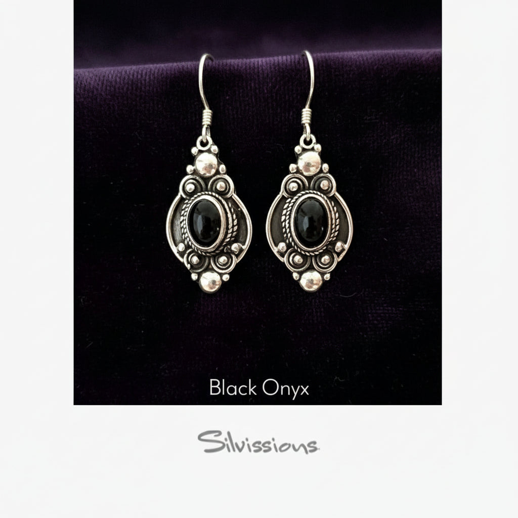 Silver earrings with black stones on a textured beige background, featuring the brand 'Silvissions'.