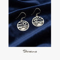 Silver earrings with a design on a blue fabric background, branded 'Silvissions'.