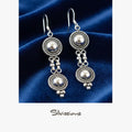 Silver earrings with spherical designs on a blue fabric background, branded 'Silvissions'.