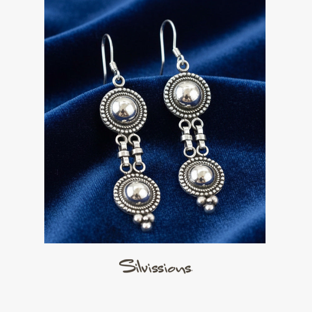 Silver earrings with spherical designs on a blue fabric background, branded 'Silvissions'.