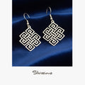Pair of silver earrings with geometric design on a blue fabric background, branded 'Silvissions'.