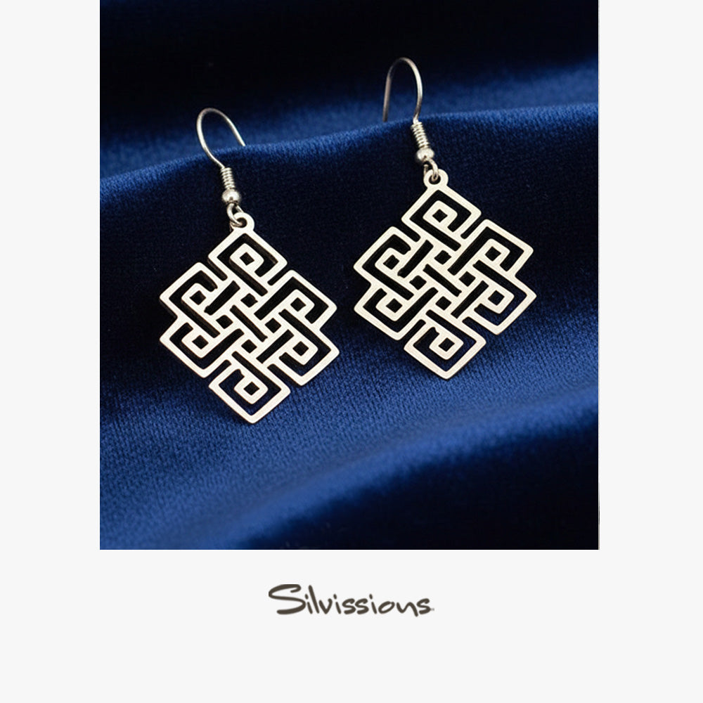 Pair of silver earrings with geometric design on a blue fabric background, branded 'Silvissions'.