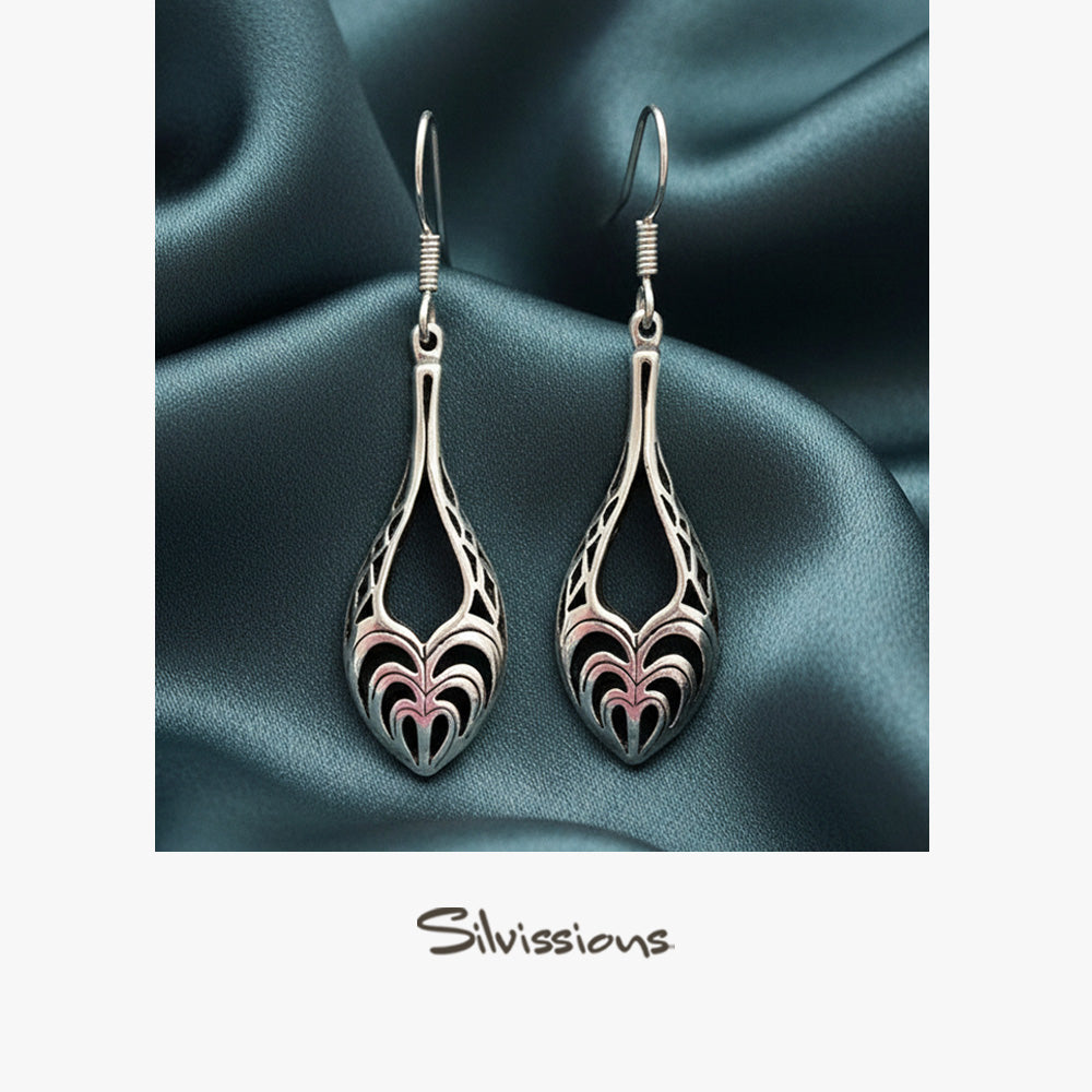 Pair of silver earrings with intricate designs on a teal fabric background, featuring the brand 'Silvissions'.
