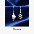 Silver earrings with geometric design on a blue satin background, branded 'Silviissions'.
