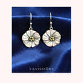 Silver floral earrings with gold centers on a beige background, branded 'Silvissions'.