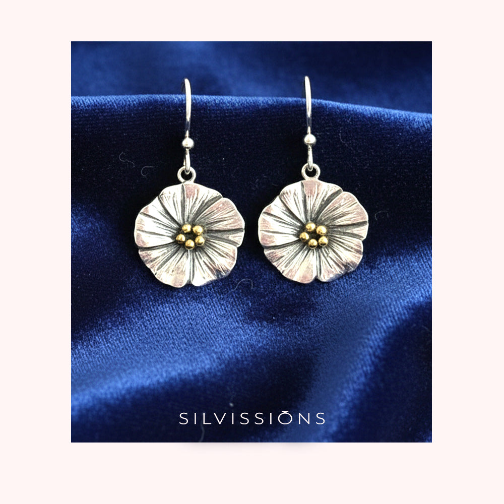 Silver floral earrings with gold centers on a beige background, branded 'Silvissions'.