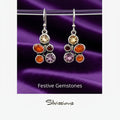 Pair of earrings with colorful gemstones on a blurred background, featuring the brand 'Silvissions'.