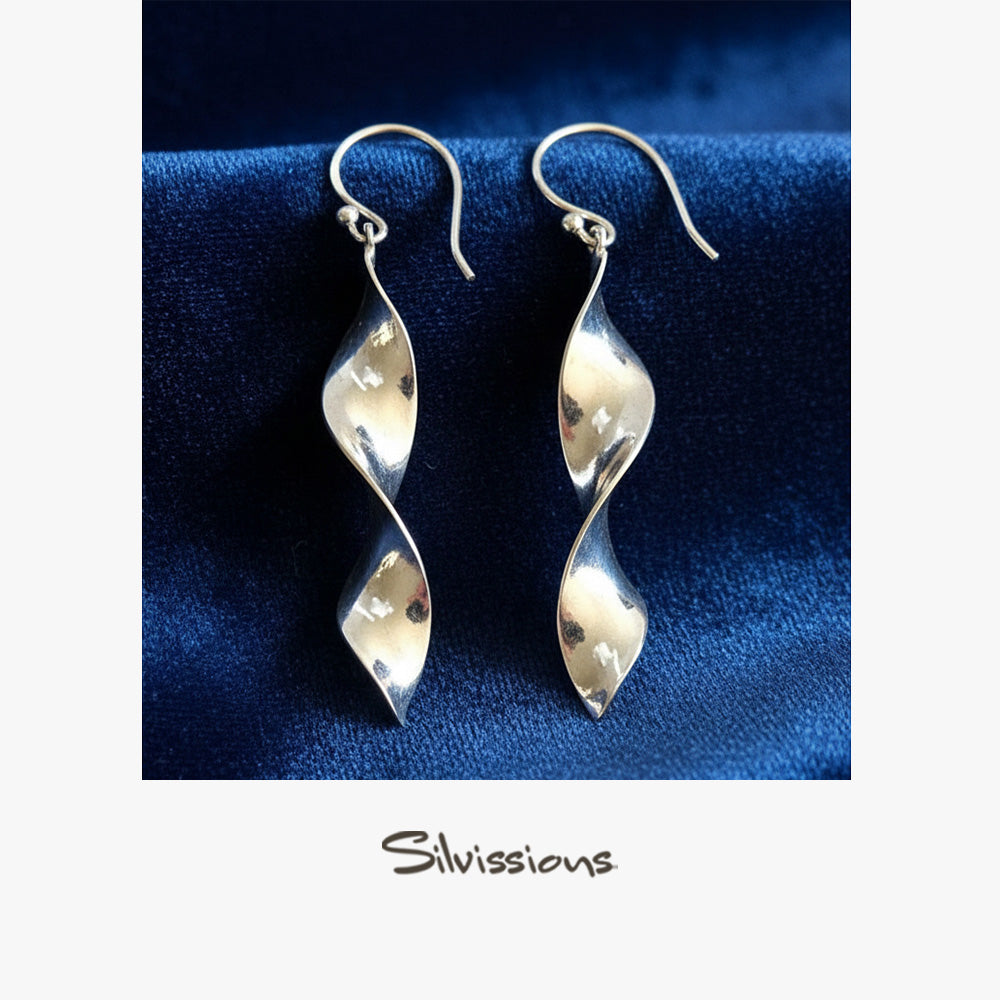 Silver spiral earrings on a blue fabric background with 'Silvissions' branding.