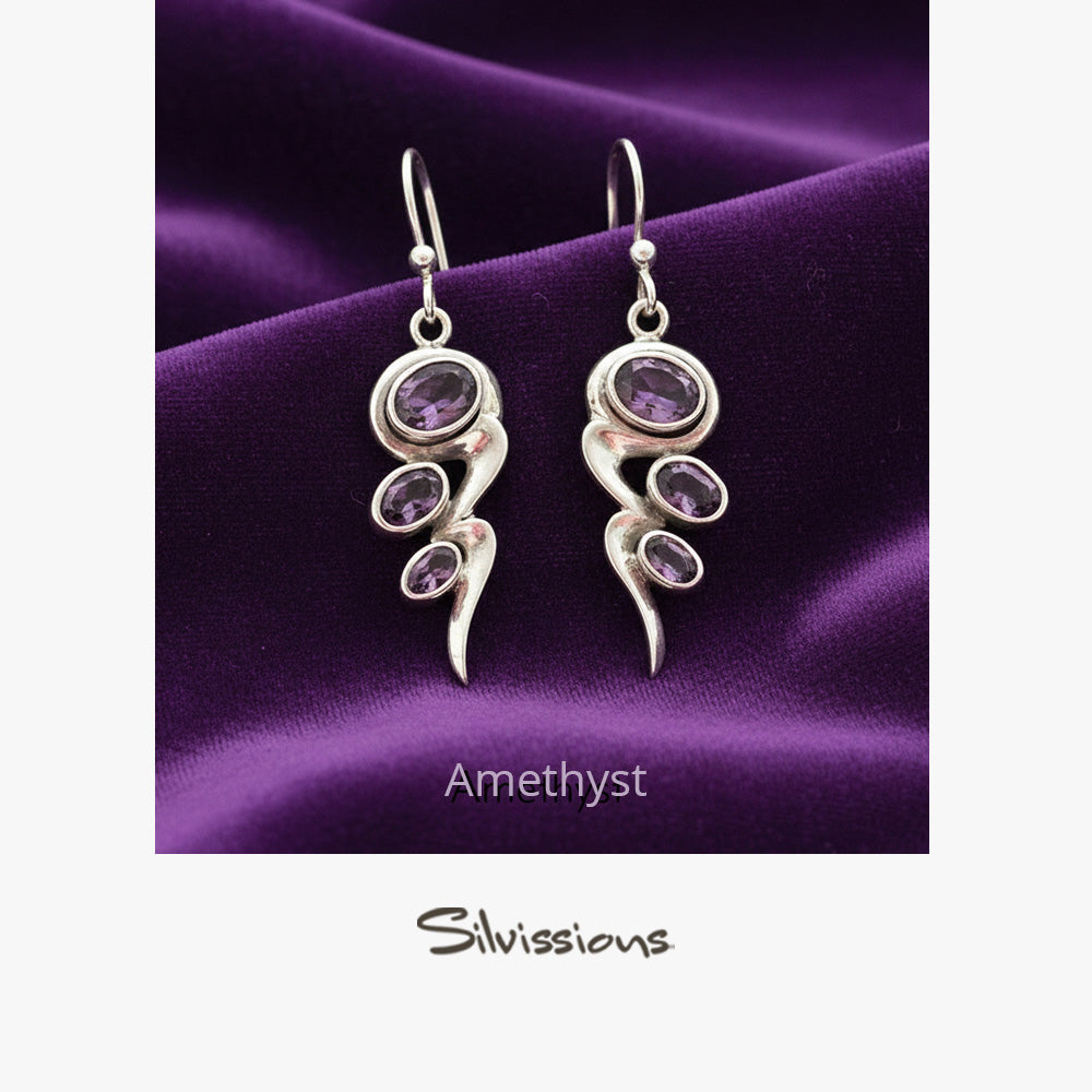 Silver earrings with purple gemstones on a purple fabric background, featuring the brand 'Silvissions'.
