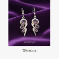 Silver earrings with purple gemstones on a purple fabric background, featuring the brand 'Silvissions'.