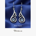 Silver earrings with blue gemstones on a blue fabric background, featuring the brand 'Silvissions'.