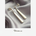 Silver earrings with long, thin pendants on a gray fabric background, branded 'Silvissions'.