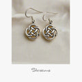 A pair of sterling silver dangle earrings with an intricate knot design, displayed against a light background.