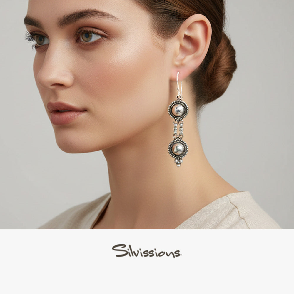 Close-up of a woman wearing a silver dangle earring on a neutral background, featuring the Silvassions brand.